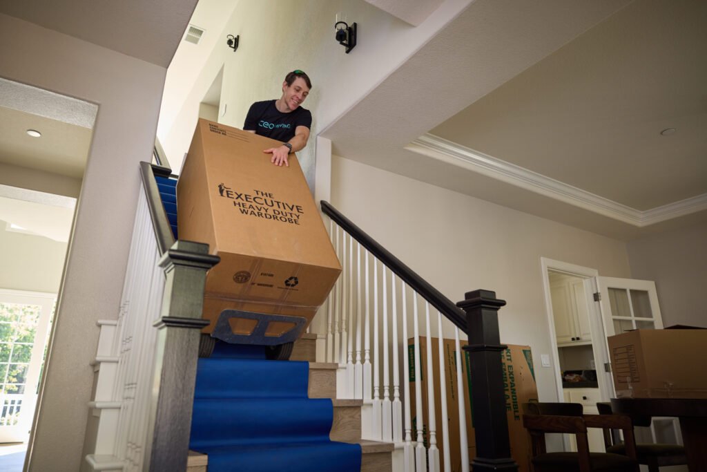Mover carrying a box down carpeted stairs, the same protected route used when moving a piano
